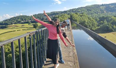 People standing beside water and smiling with their arms open wide.