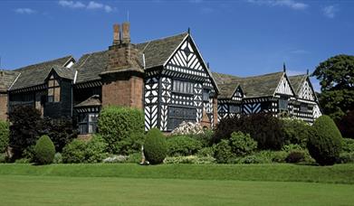 Outside of Speke Hall with green grass and trees.