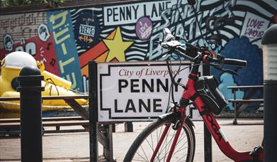 A street sign that says 'Penny Lane' with a bicycle in front of it.